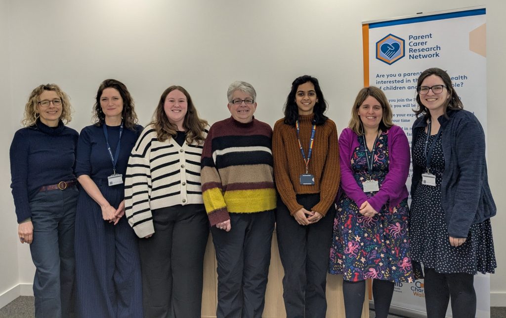 Alt text: A photograph of 7 women standing in a row next to the Parent Carer Research Network banner. These women are the team behind the network: Polly Waite, Emily Lloyd, Emily Wyatt, Nikki Chapman, Shanta Raj, Susannah Dodds and Heather Dyer.